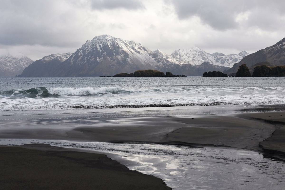 Surf rolling in beneath snowy peaks